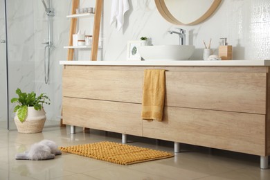 Photo of Soft orange bath mat and slippers on floor in bathroom