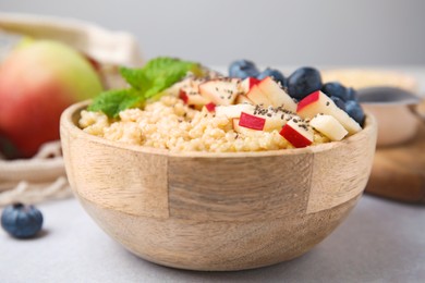 Bowl of delicious cooked quinoa with apples, blueberries and chia seeds on light grey table, closeup