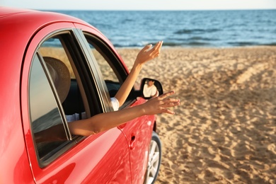 Photo of Woman and her daughter waving from car on beach, closeup. Summer trip