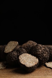 Whole and cut truffles on wooden table against black background