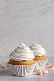 Photo of Delicious cupcakes with cream and marshmallows on white wooden table. Space for text