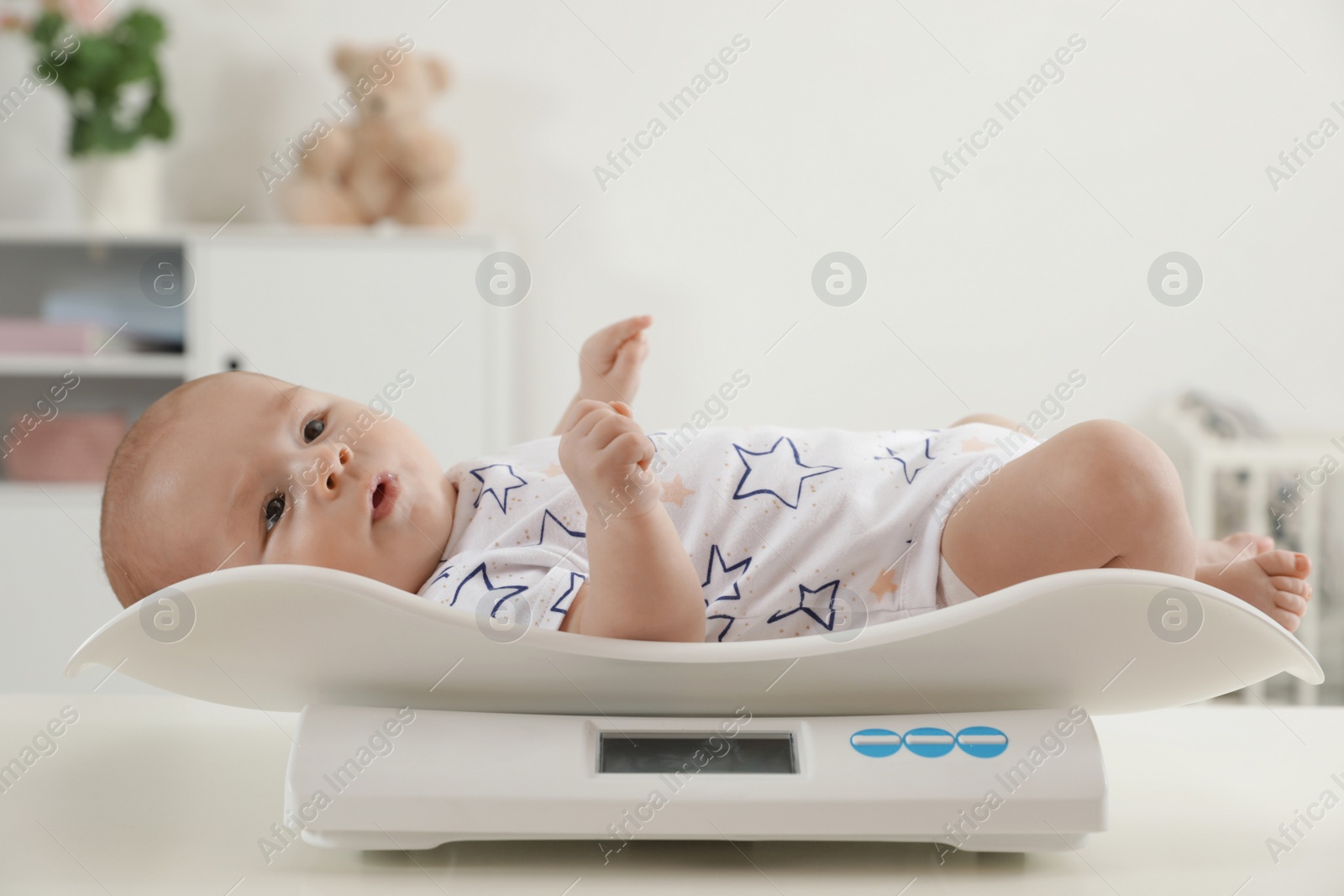 Photo of Cute little baby lying on scales in light room