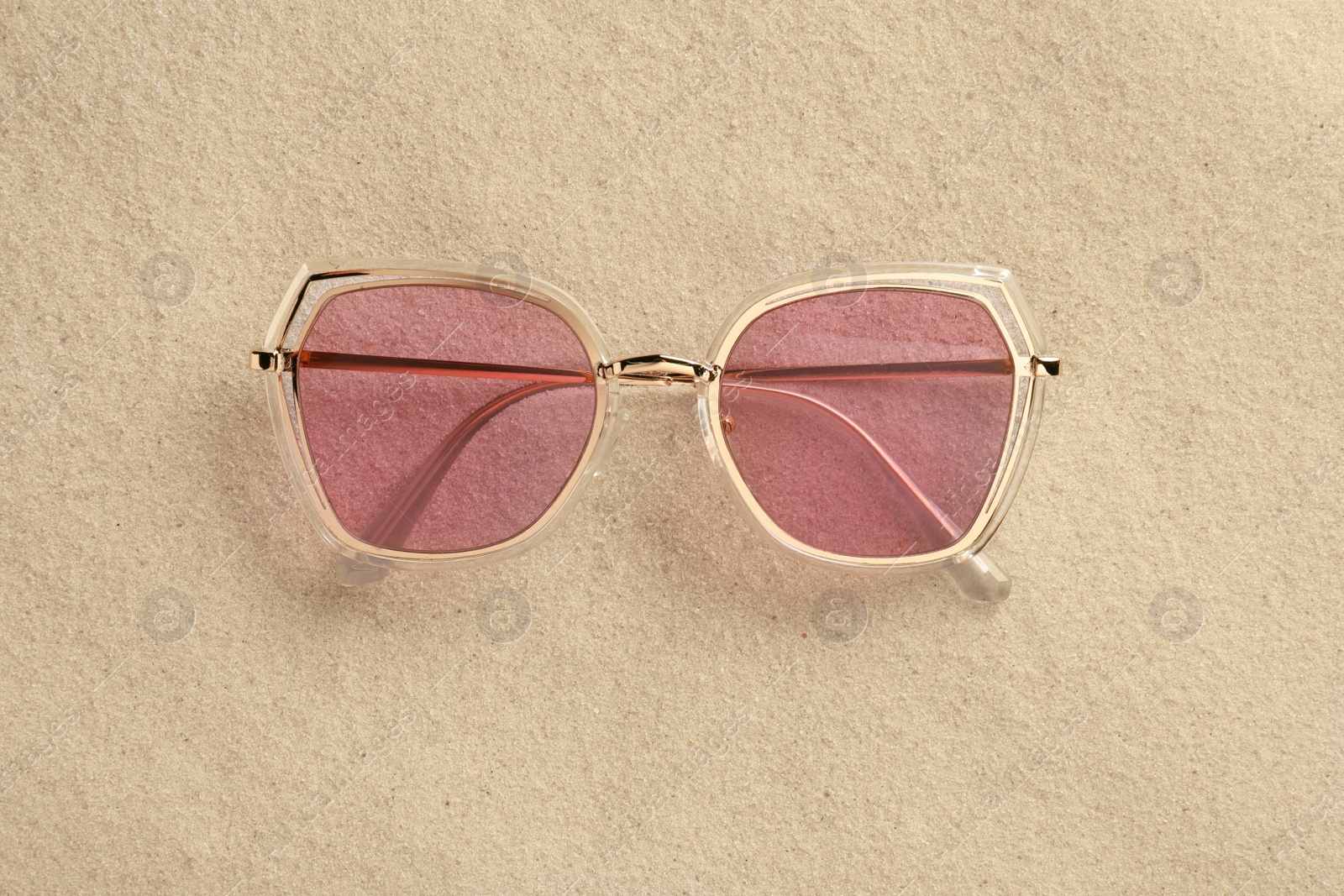 Photo of New stylish sunglasses on sand, top view