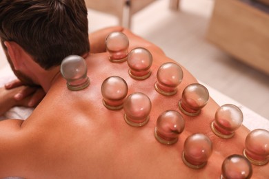 Photo of Cupping therapy. Man with glass cups on massage couch in spa salon, closeup