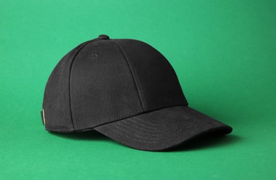 Stylish black baseball cap on green background