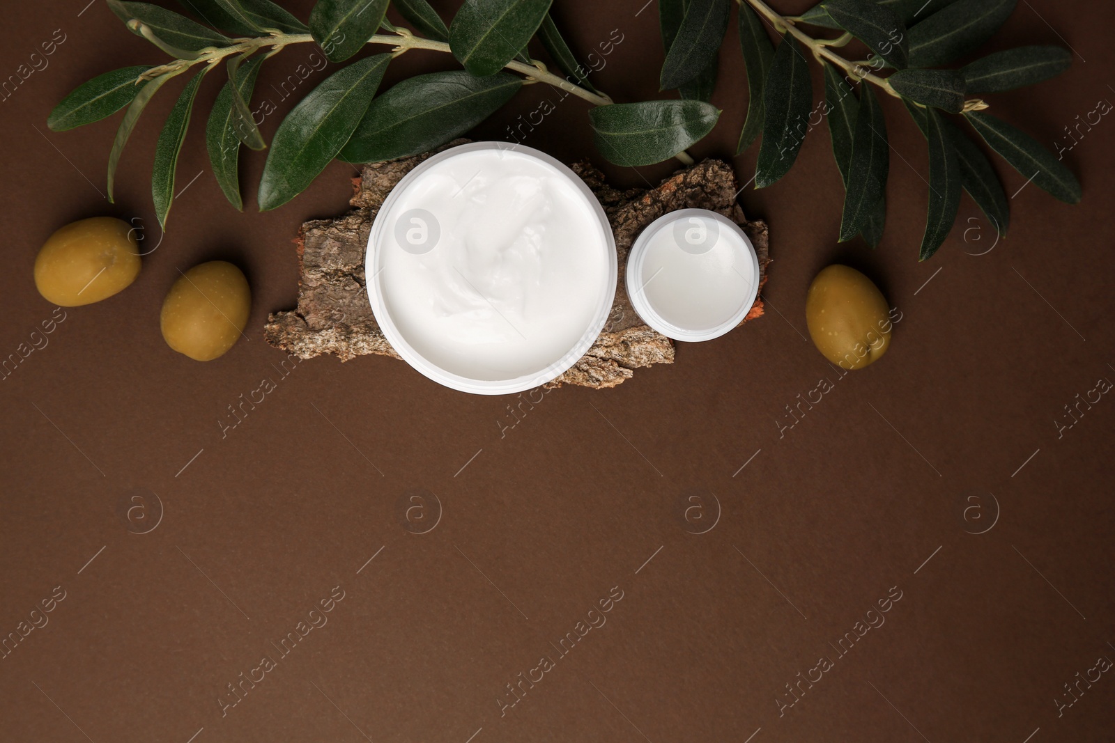 Photo of Flat lay composition with jars of cream and olives on brown background. Space for text