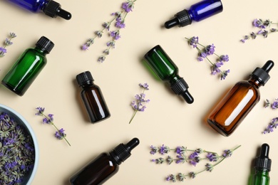 Photo of Bottles of essential oil and lavender flowers on beige background, flat lay