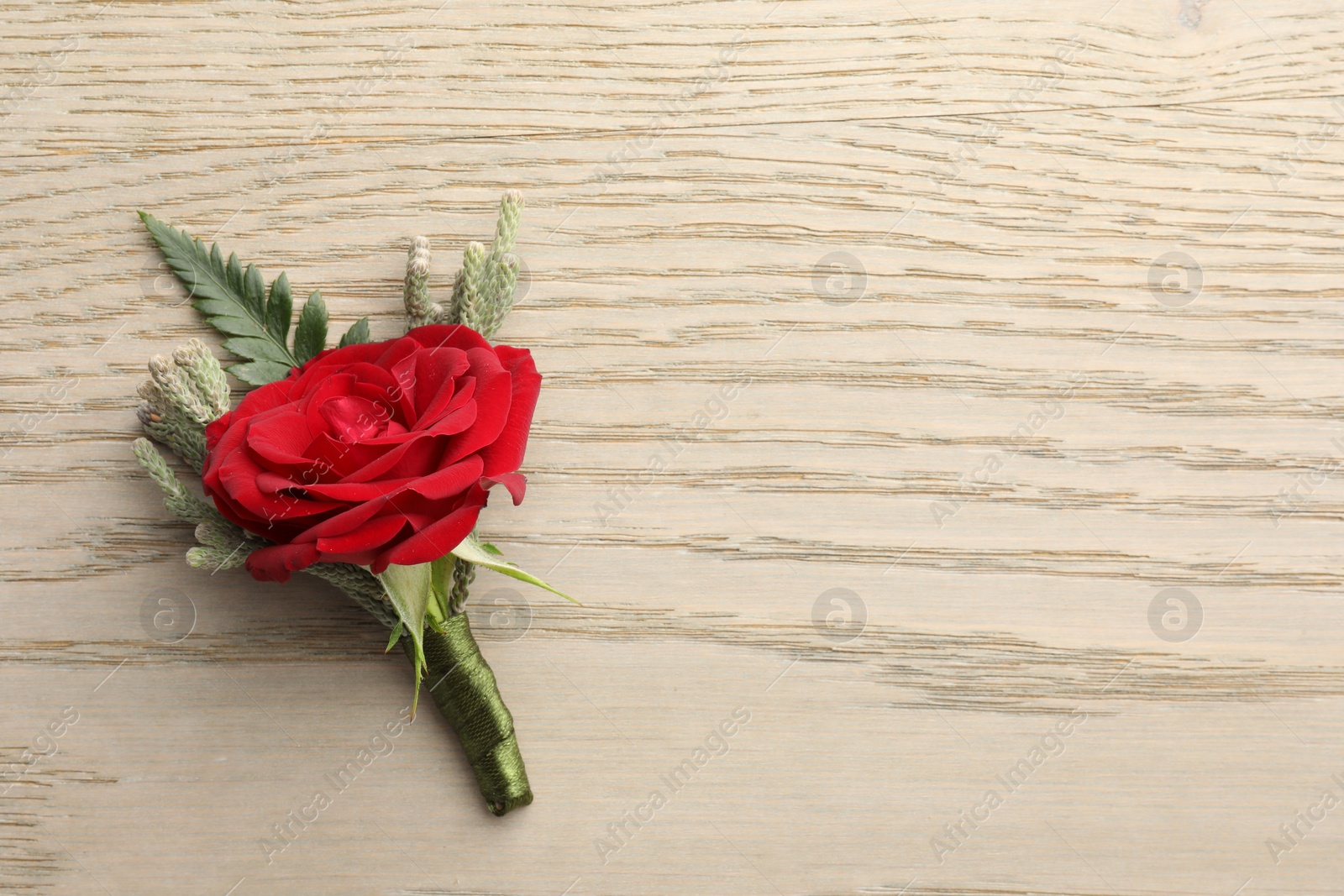 Photo of One stylish red boutonniere on light wooden table, top view. Space for text