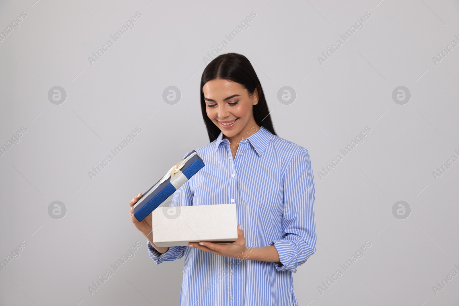 Photo of Happy young woman opening gift box on light grey background