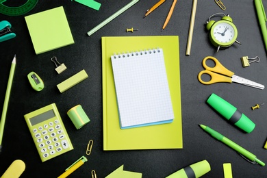 Different bright school stationery and blank notebook on black background, flat lay. Space for text