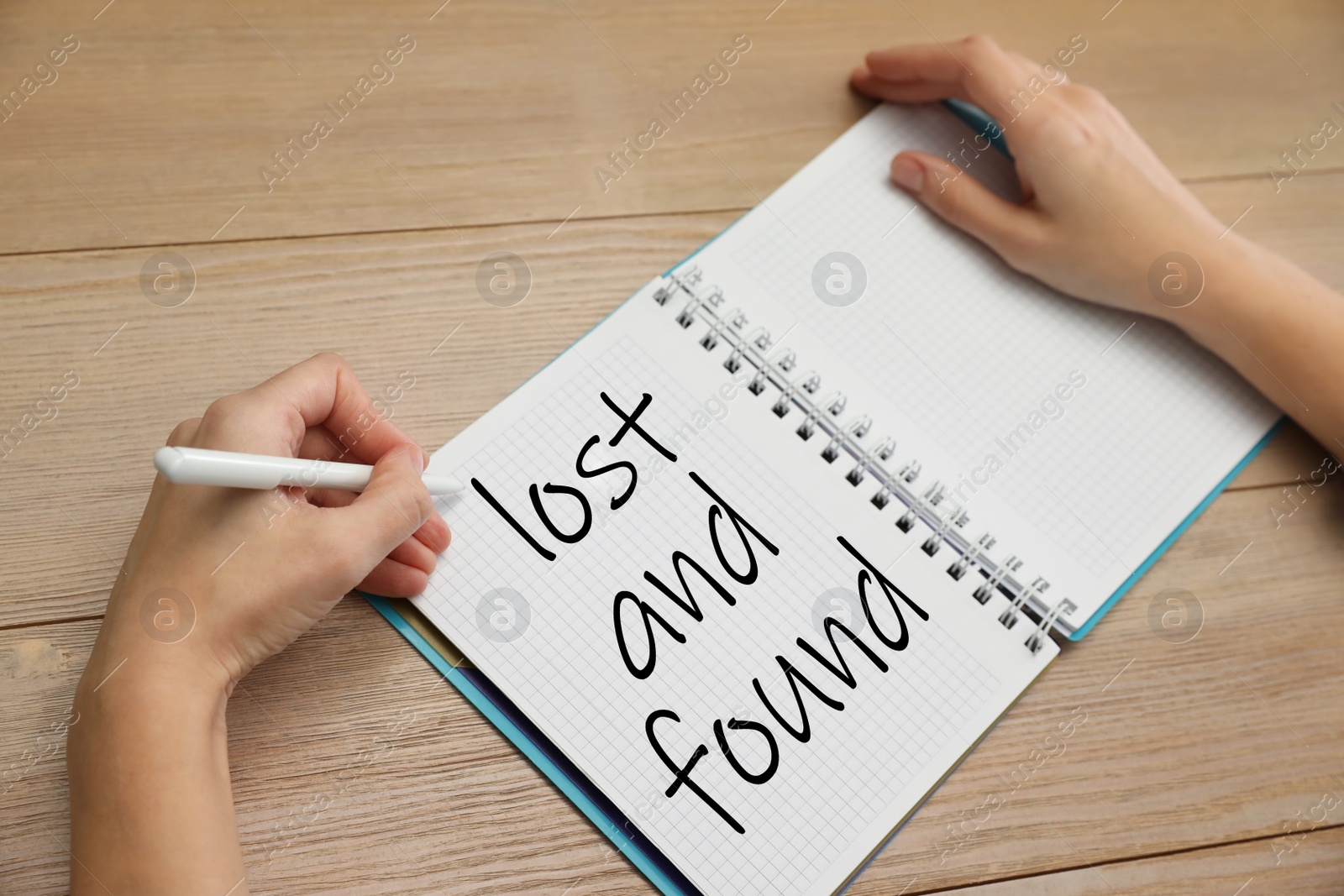Image of Woman writing phrase Lost and Found in notebook at wooden table, closeup