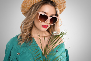 Young woman wearing stylish sunglasses and hat on light grey background