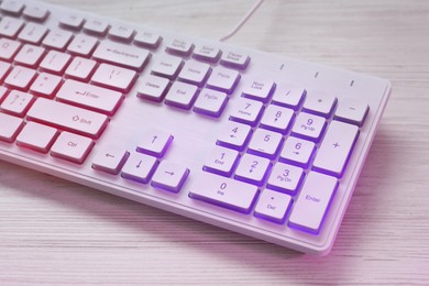 Photo of Modern RGB keyboard on white wooden table, closeup