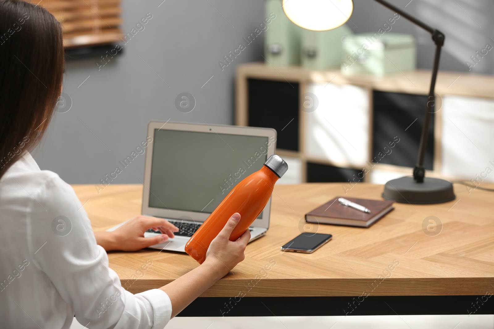 Photo of Young woman with modern thermos bottle at workplace, back view