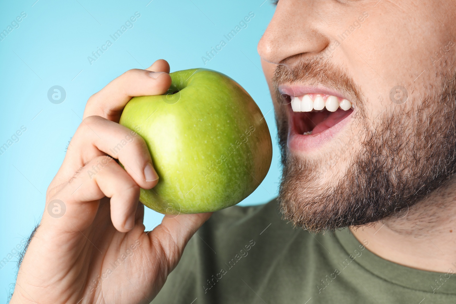 Photo of Young man with healthy teeth and apple on color background, closeup