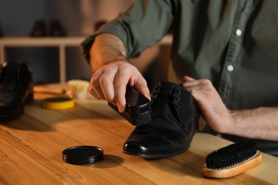 Photo of Man taking professional care of black leather shoes in workshop, closeup