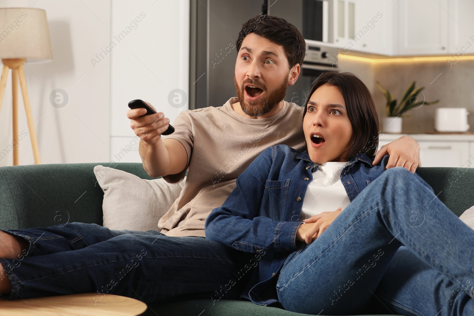 Photo of Surprised couple watching TV on sofa at home