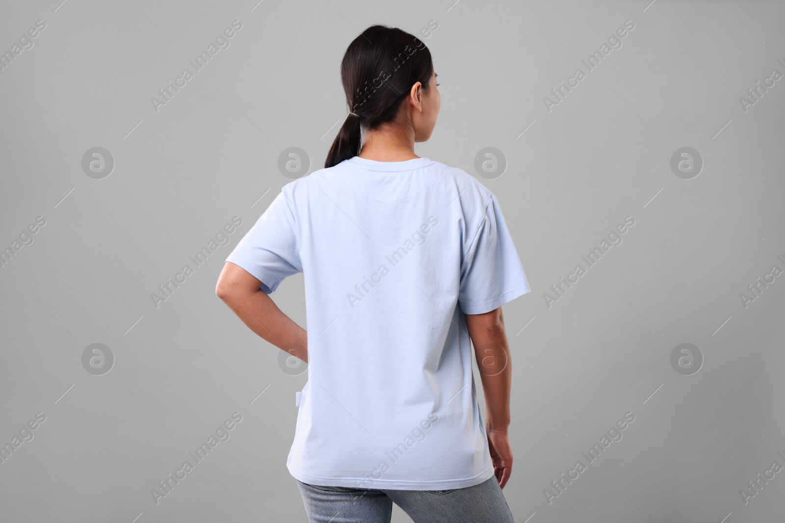 Photo of Woman wearing light blue t-shirt on grey background, back view