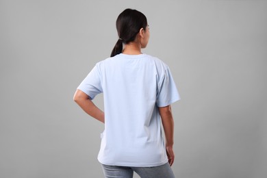 Woman wearing light blue t-shirt on grey background, back view
