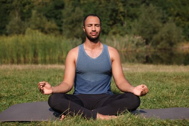 Photo of Man practicing yoga on mat outdoors. Lotus pose