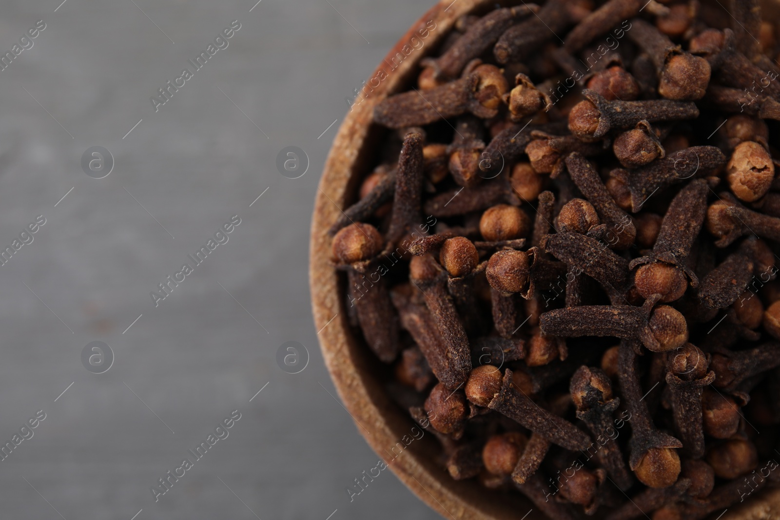 Photo of Aromatic cloves in bowl on grey table, top view. Space for text