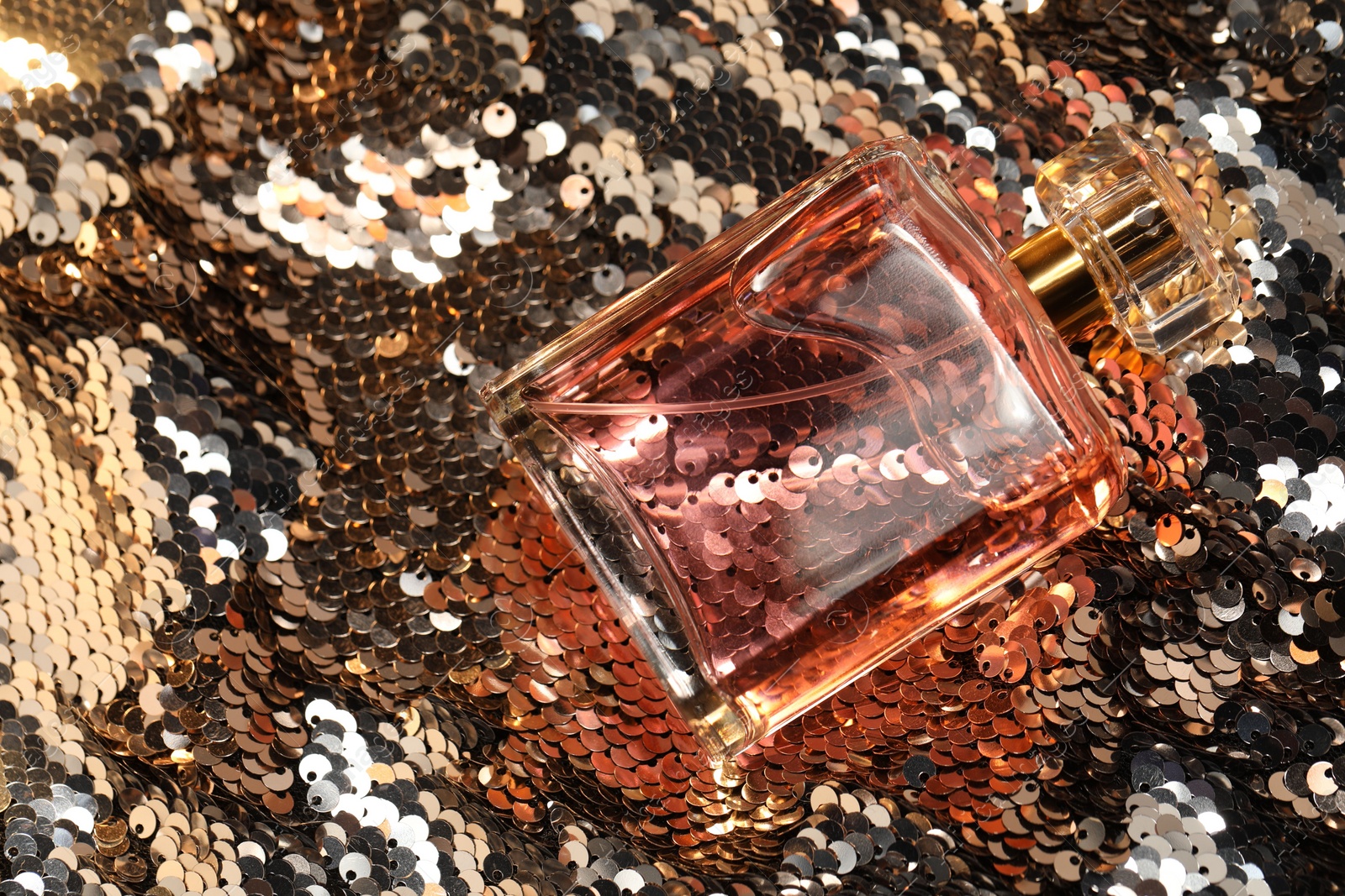 Photo of Luxury perfume in bottle on fabric with silver sequins, top view
