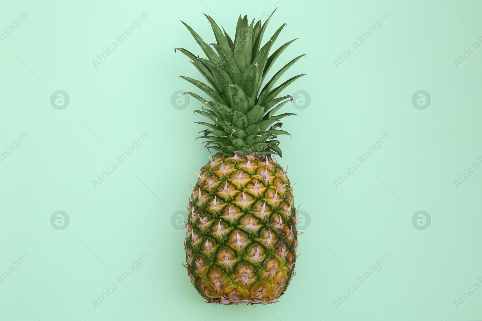 Photo of Whole ripe pineapple on light green background, top view