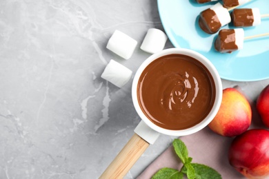 Photo of Fondue pot and marshmallow dipped into milk chocolate on light table, flat lay. Space for text