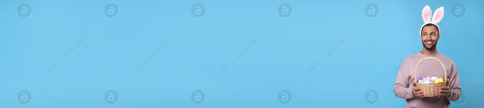 Image of Man with bunny ears holding basket full of Easter eggs on light blue background, space for text. Banner design