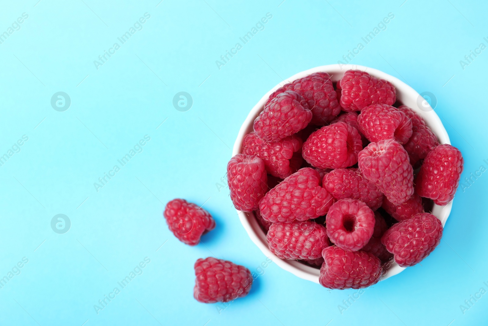 Photo of Bowl of delicious ripe raspberries on blue background, top view. Space for text