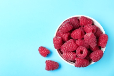 Photo of Bowl of delicious ripe raspberries on blue background, top view. Space for text