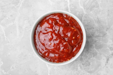 Photo of Bowl of hot chili sauce on marble background, top view