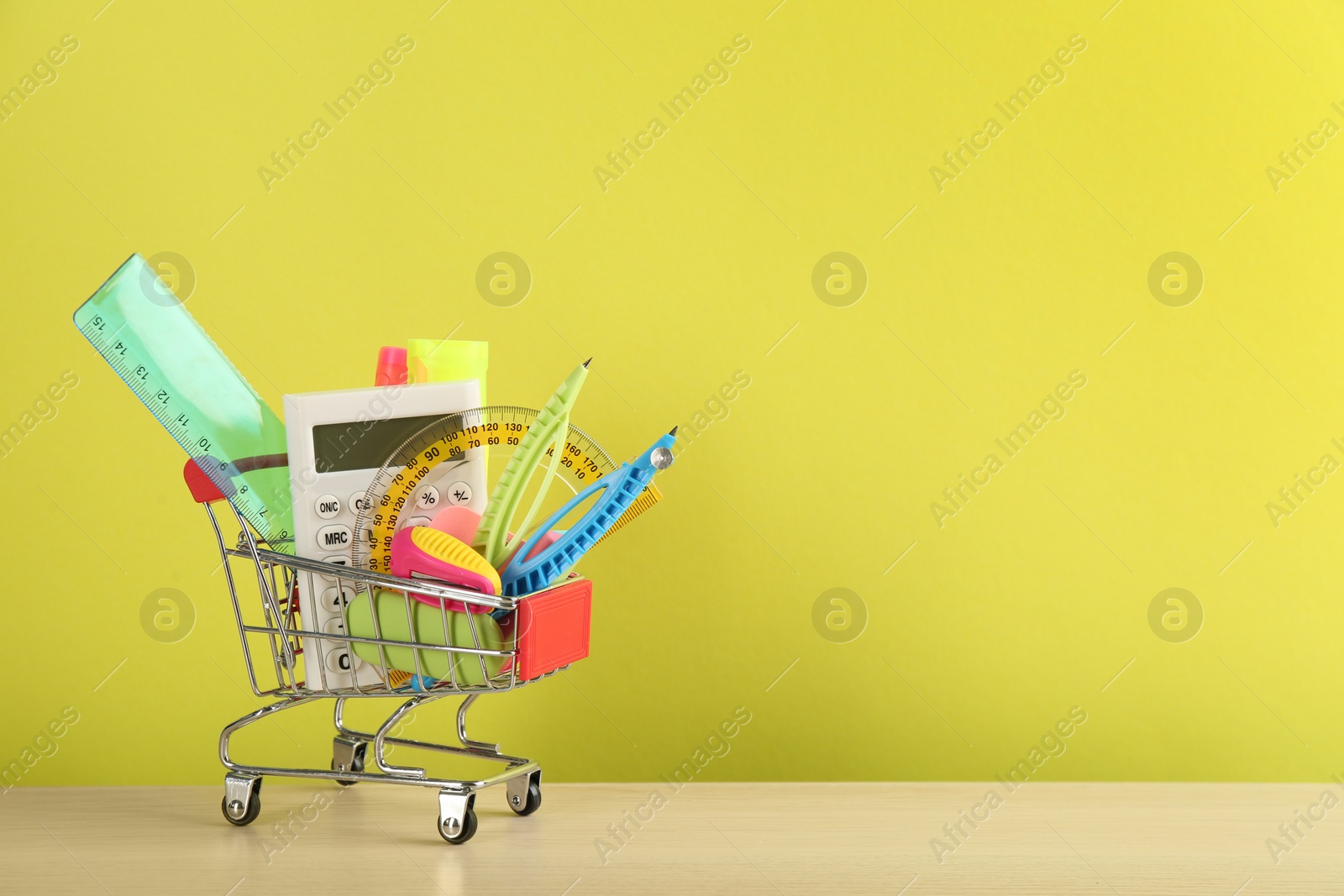 Photo of Different school stationery in miniature shopping cart on table against yellow background, space for text. Back to school