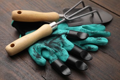 Photo of Claw gardening gloves, trowel and rake on wooden table, closeup
