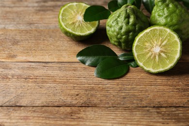 Photo of Fresh ripe bergamot fruits with green leaves on wooden table, space for text