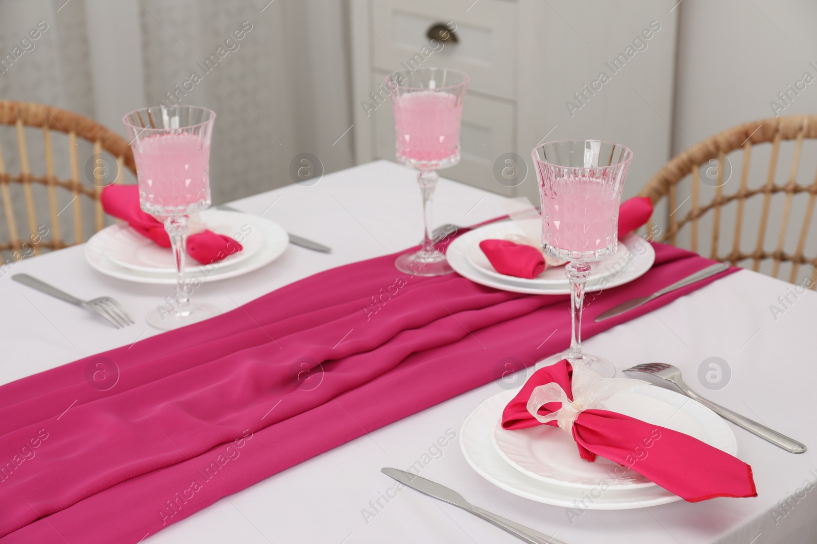 Photo of Table setting. Glasses of tasty beverage, plates with pink napkins and cutlery in dining room