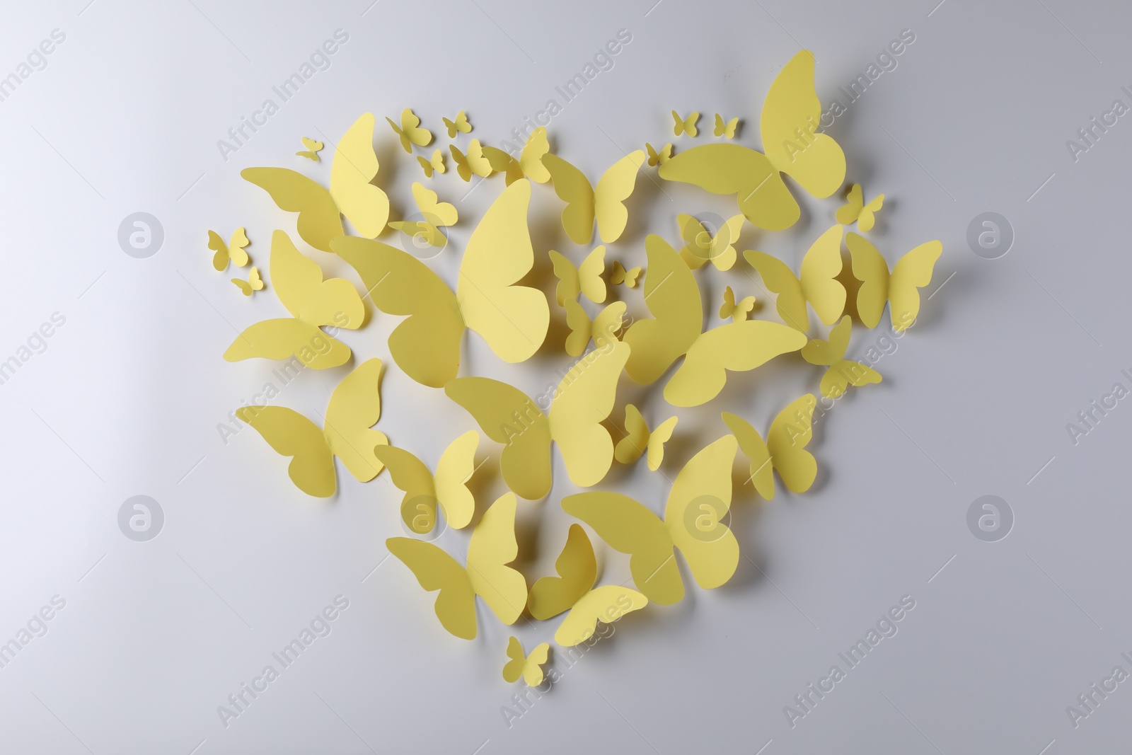 Photo of Heart shape made of yellow paper butterflies on white background, top view