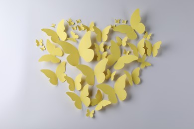 Photo of Heart shape made of yellow paper butterflies on white background, top view