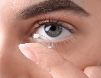 Photo of Young woman putting contact lens in her eye, closeup