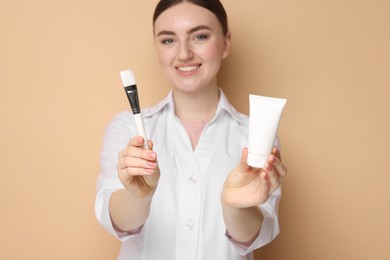 Cosmetologist with cosmetic product and brush on beige background, selective focus