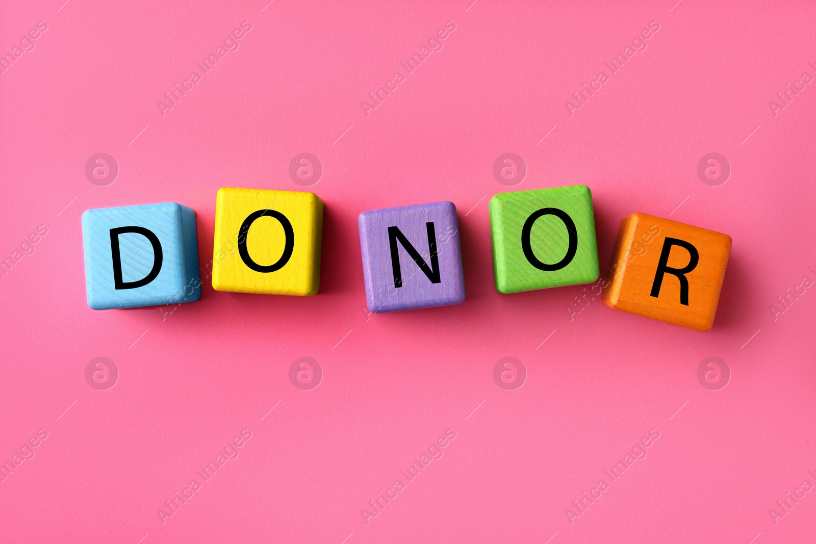 Photo of Word Donor made of colorful wooden cubes on pink background, flat lay