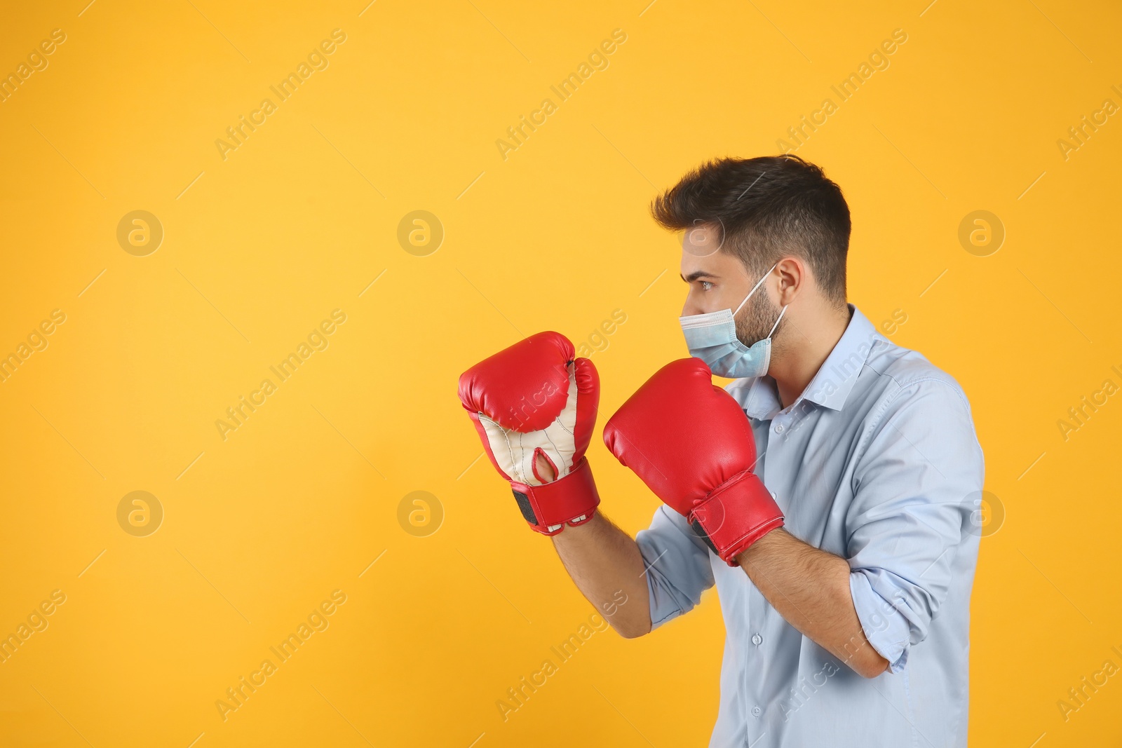 Photo of Man with protective mask and boxing gloves on yellow background, space for text. Strong immunity concept