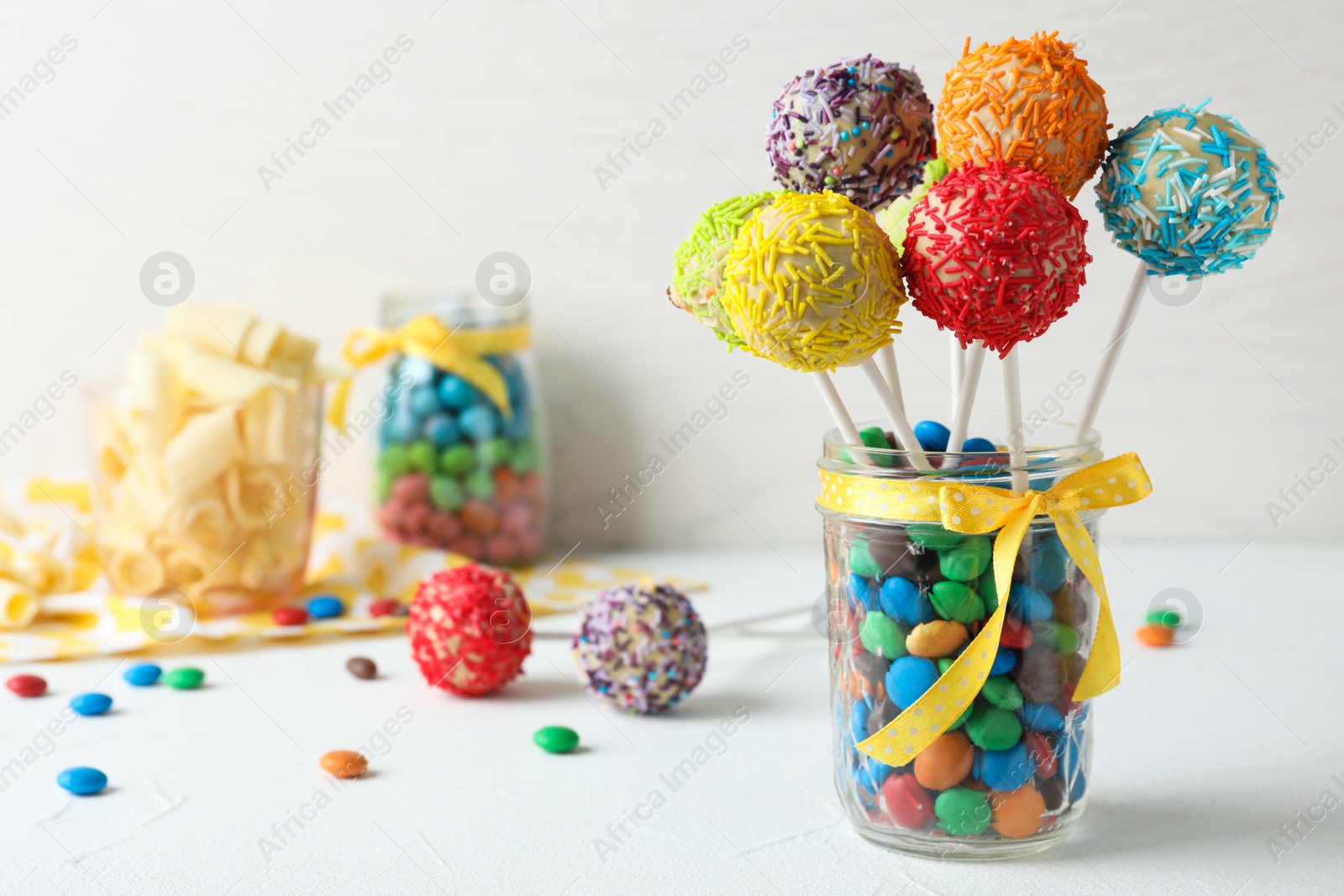 Photo of Yummy bright cake pops in glass jar full of candies on table. Space for text