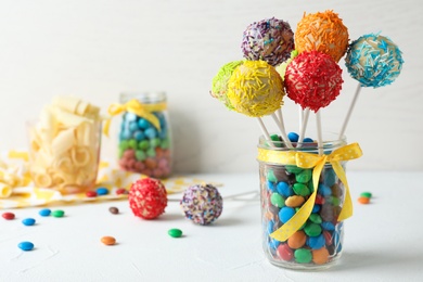 Photo of Yummy bright cake pops in glass jar full of candies on table. Space for text