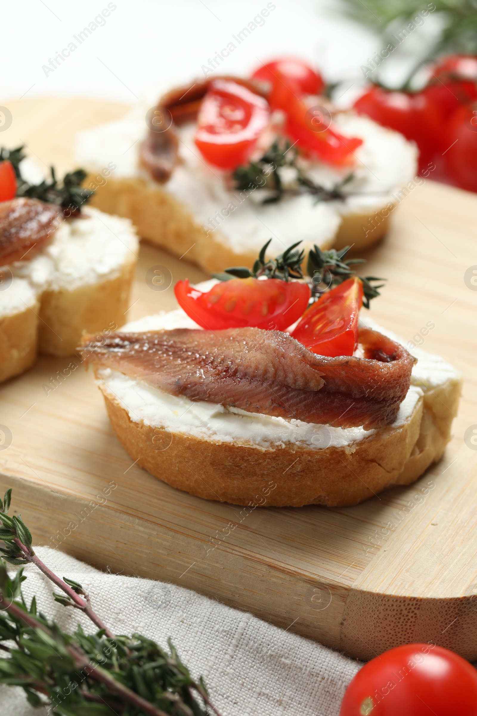 Photo of Delicious sandwiches with cream cheese, anchovies and tomatoes on wooden board, closeup