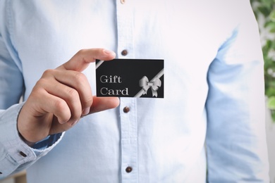 Photo of Man with gift card on blurred background, closeup