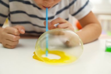 Photo of Little boy blowing slime bubble on white table, closeup