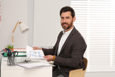 Businessman putting document into punched pocket at white table in office
