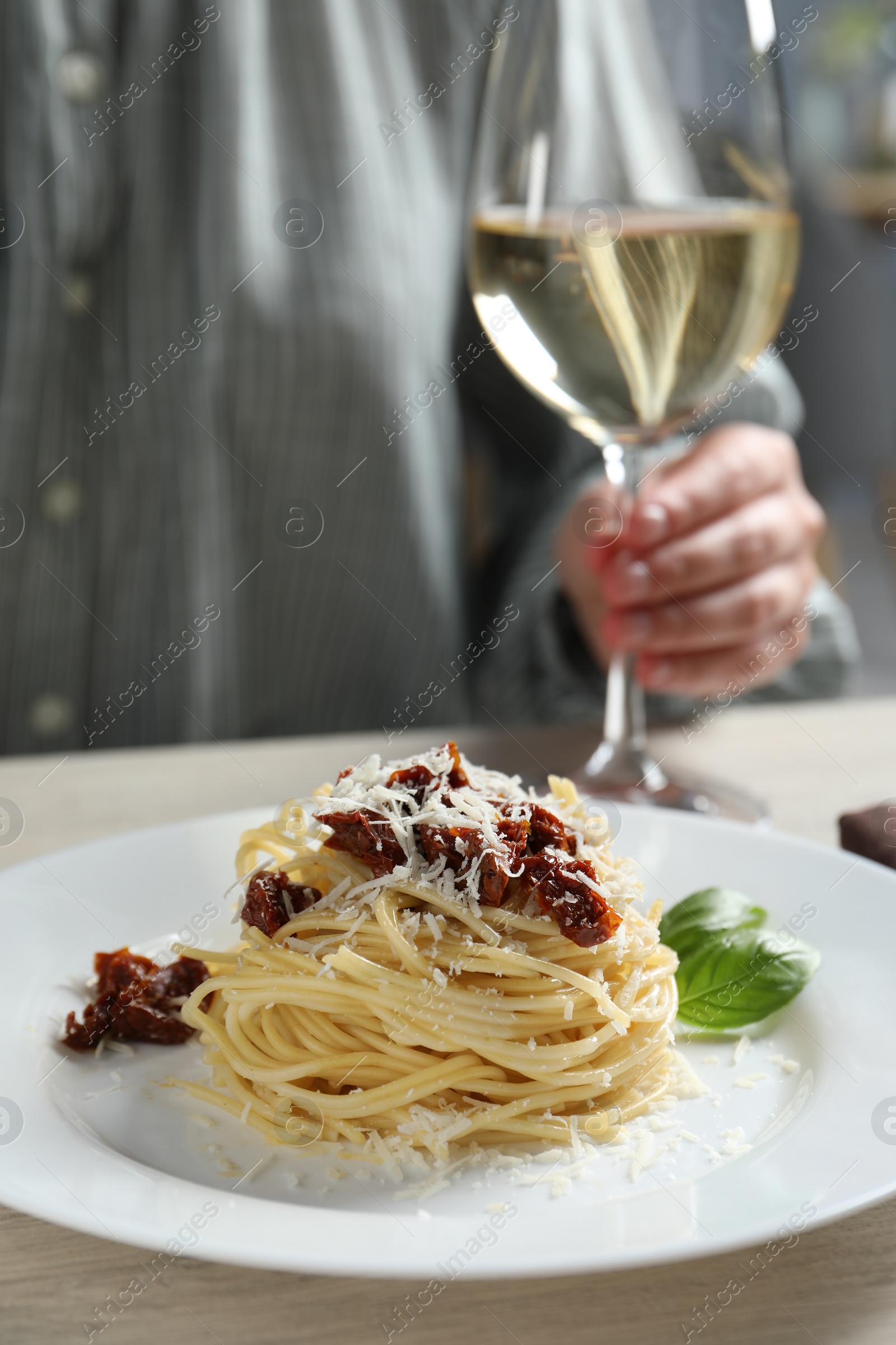 Photo of Woman enjoying tasty spaghetti with sun-dried tomatoes and parmesan cheese and wine at wooden table in restaurant, closeup. Exquisite presentation of pasta dish