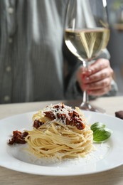 Woman enjoying tasty spaghetti with sun-dried tomatoes and parmesan cheese and wine at wooden table in restaurant, closeup. Exquisite presentation of pasta dish